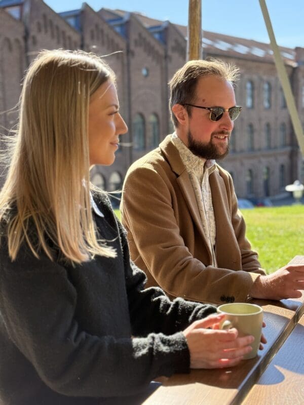 Två personer som sitter vid en bänk och dricker kaffe i solen